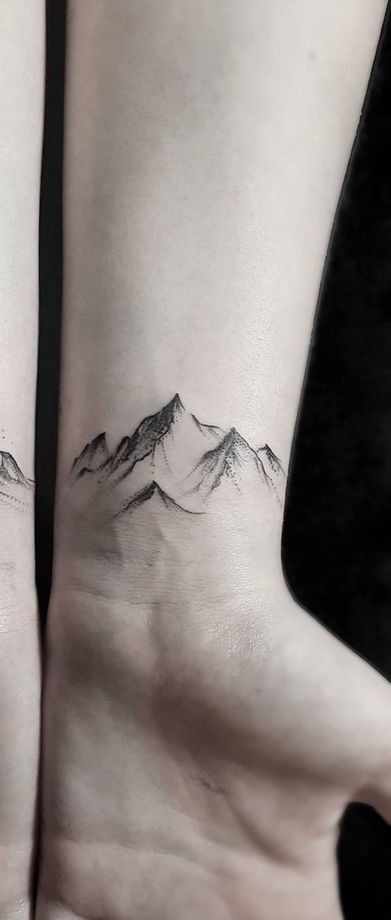 a small mountain tattoo on the left side of the arm, with snow capped mountains in the background