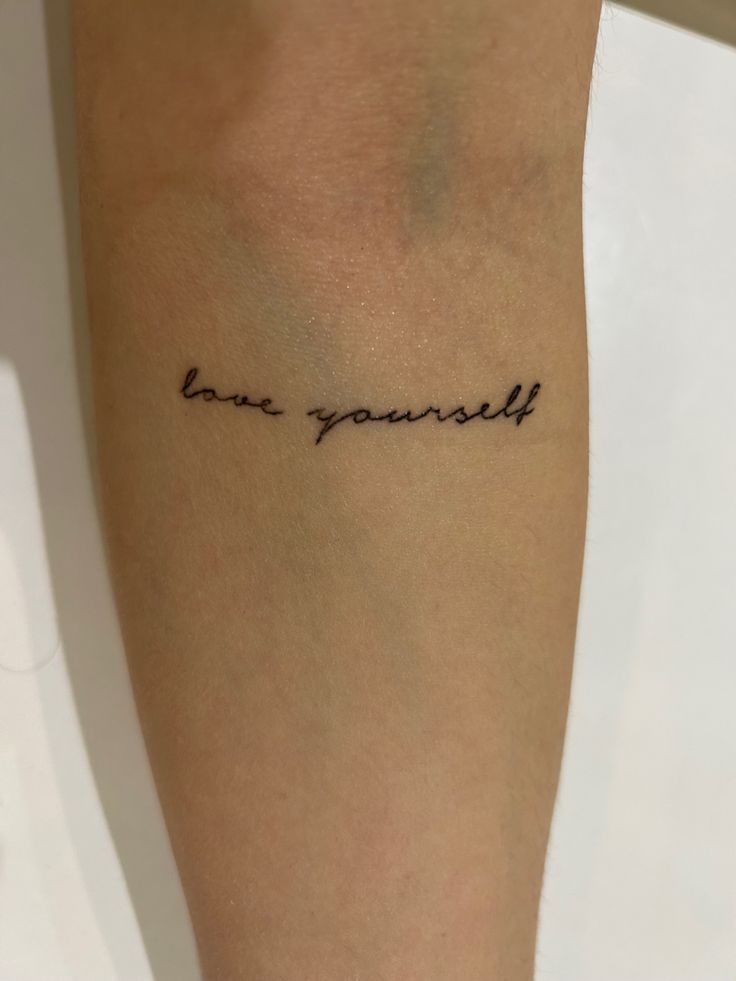 a woman's arm with the word love yourself written on it, in cursive font