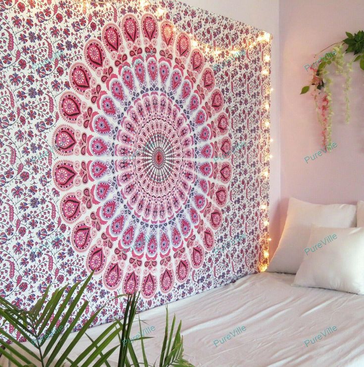 a pink and white wall hanging on the side of a bed in a room with plants