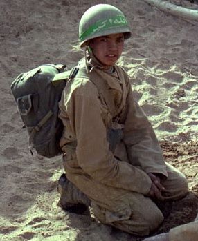 a young boy wearing a helmet sitting in the sand