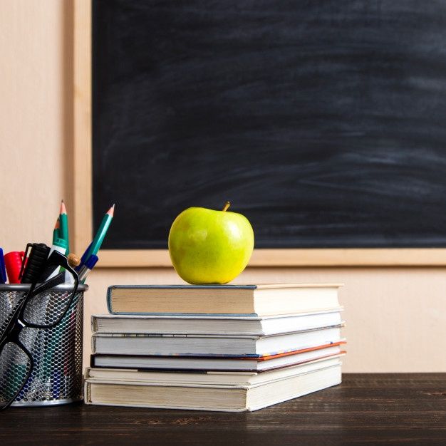 an apple sitting on top of books next to a cup with pens and pencils