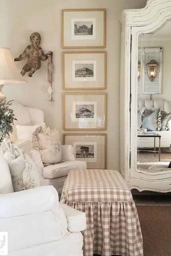 a living room filled with white furniture and pictures on the wall above it's mirror