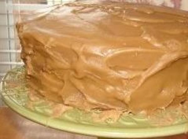 a chocolate cake with frosting sitting on top of a green plate in front of a window