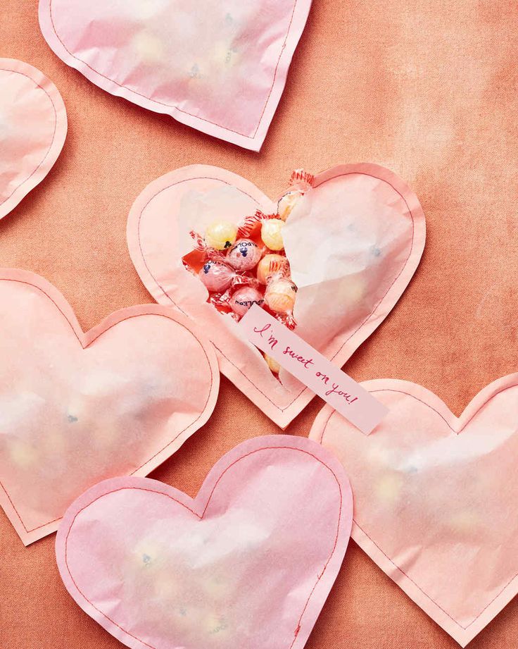 four heart shaped candy bags on top of a pink cloth covered table with candies in them