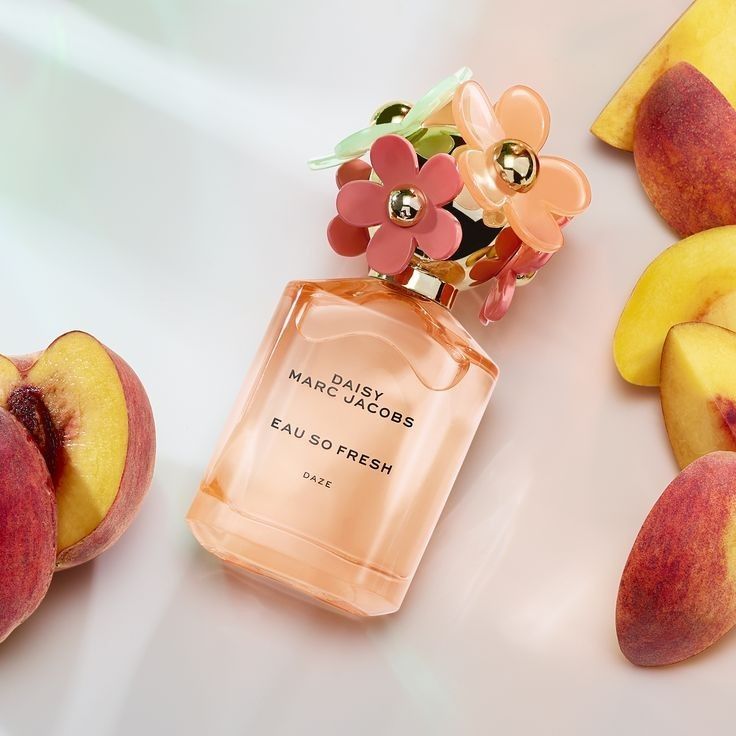 a bottle of perfume next to peaches on a white surface with fruit around it