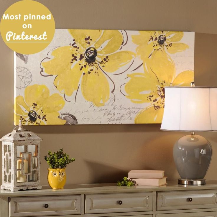 a yellow flowered painting hangs on the wall above a dresser with two lamps and a lamp shade