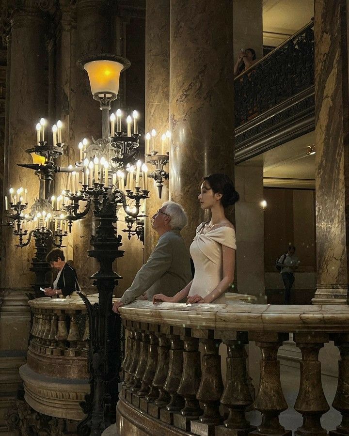 a man and woman are sitting on a balcony with chandelier in the background