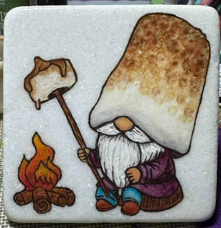 a glass tile with an image of a gnome cooking marshmallows over a campfire