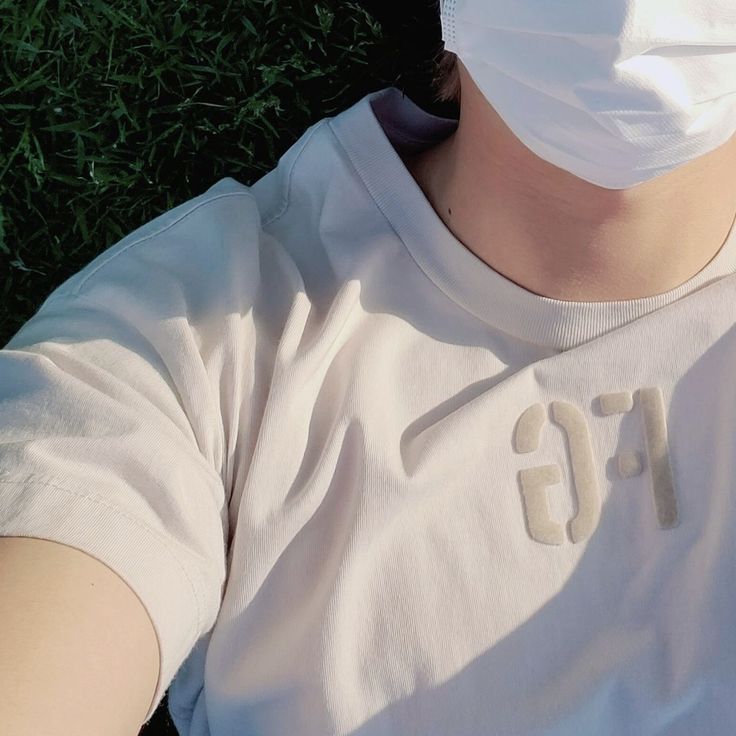 a person wearing a face mask laying in the grass with their hand on his chest