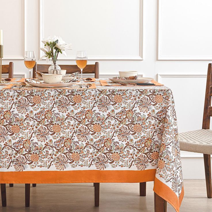 an orange and white table cloth on top of a dining room table with wine glasses