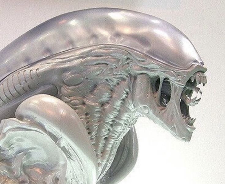 a close up of a silver object on a white surface with an alien like head