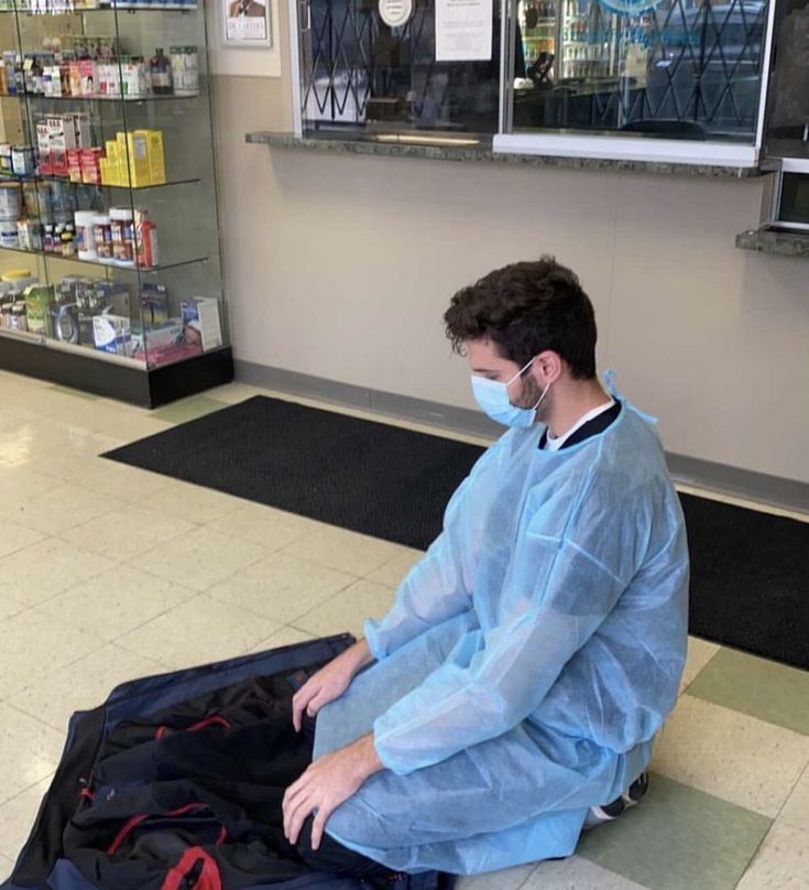 a man sitting on the floor in front of a suit case wearing a face mask