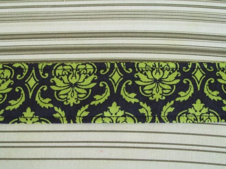 a black and green tie with an ornate design on it's side, next to a striped background