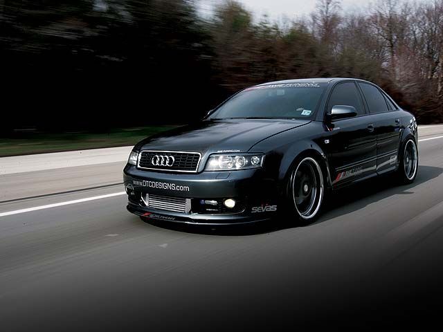 an audi car driving down the road with trees in the background