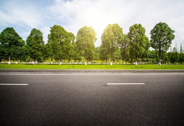 an empty road with trees and grass in the backgrouds, on a sunny day