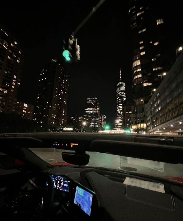 a car driving down the road at night time with city lights in the background and buildings lit up