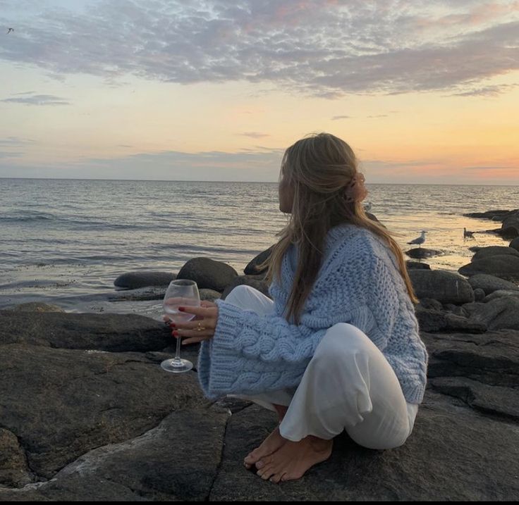 a woman is sitting on the rocks with a glass of wine in front of her