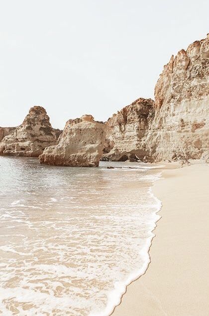 a sandy beach with waves coming in to the shore and large rocks sticking out of the water