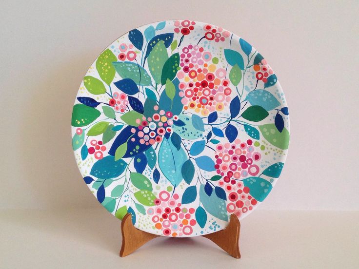 a colorful plate on a wooden stand with flowers and leaves painted on the front, sitting on a white surface