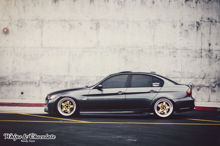 a black car with gold rims parked in front of a concrete wall and parking lot