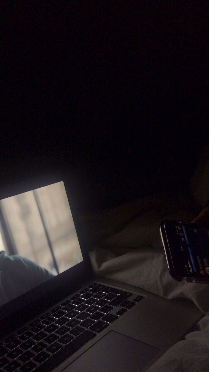 a laptop computer sitting on top of a bed next to a person holding a cell phone