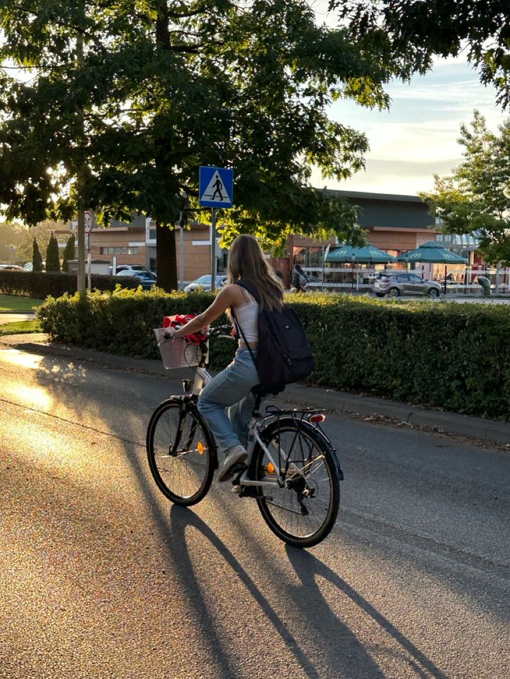 a woman riding a bike down the street with a backpack on it's back