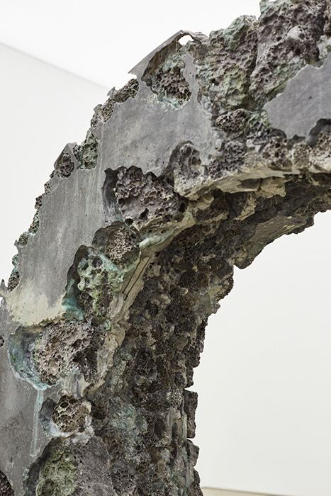 an abstract sculpture is shown in front of a white wall and grey concrete structure with green moss growing on it