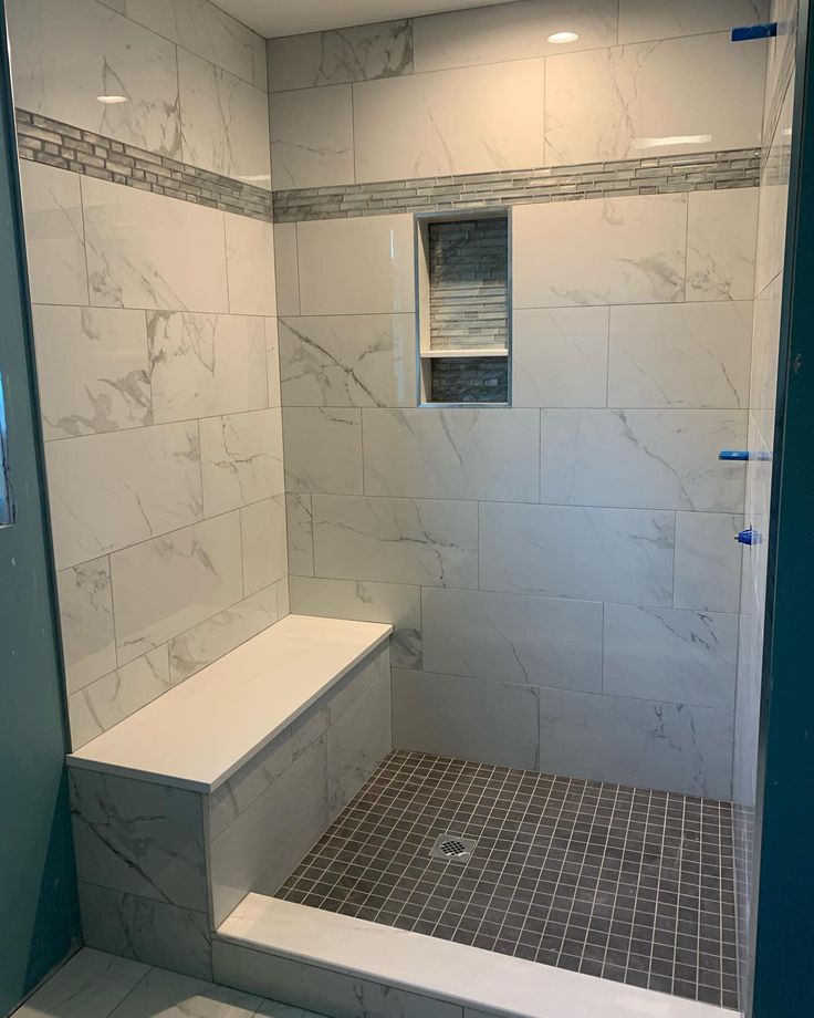 a bathroom with white marble walls and tile flooring, along with a walk in shower