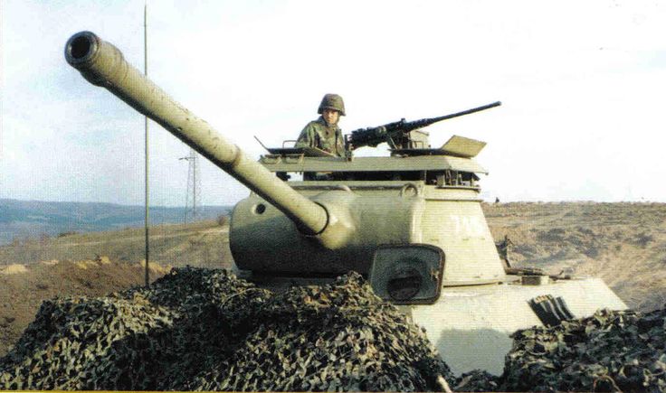 a man sitting on top of a tank in the middle of a dirt field next to a hill