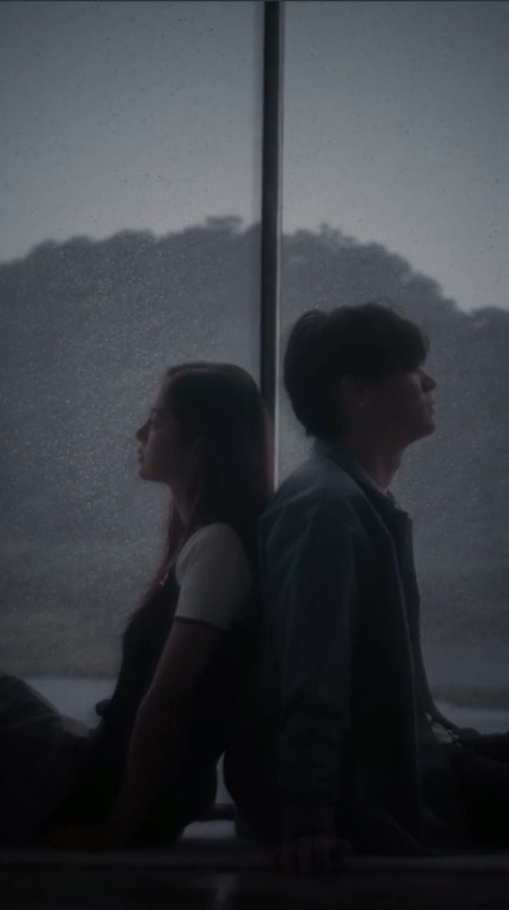 two people sitting on a window sill in the rain