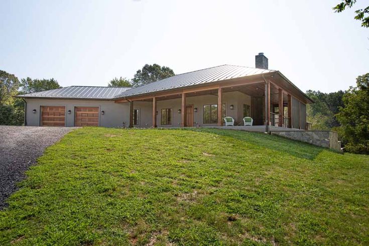 a house with a metal roof on top of a grassy hill next to a gravel road