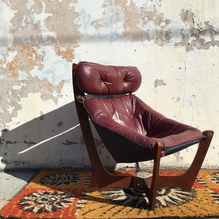 a brown leather chair sitting on top of a rug next to a cement wall with peeling paint