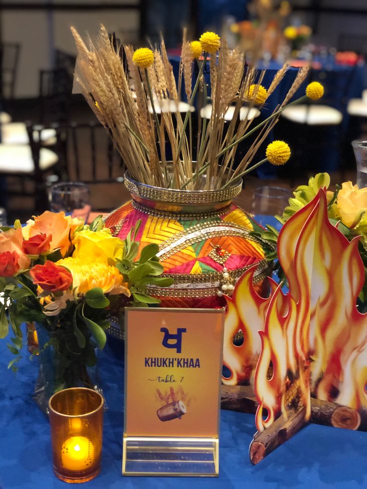 a table topped with vases filled with flowers next to cards and candles on top of a blue cloth covered table