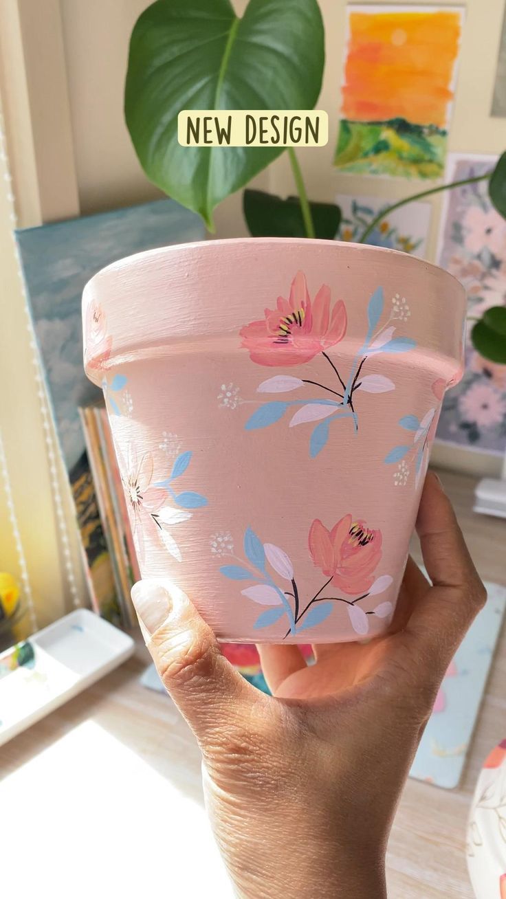 a hand holding a pink flower pot with flowers painted on it