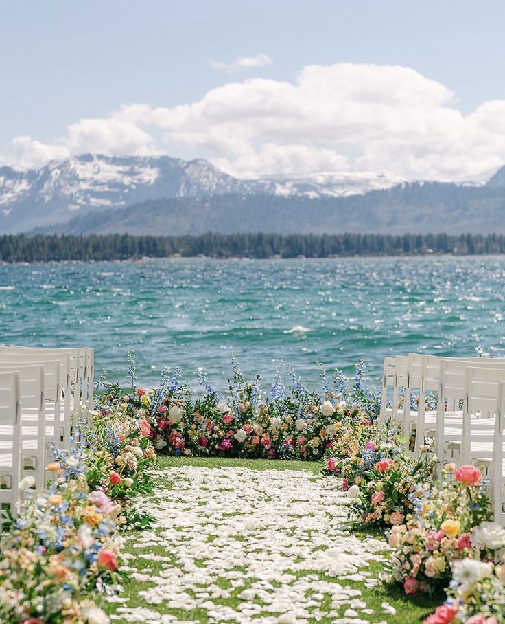 an outdoor ceremony set up by the water with flowers and greenery on the aisle