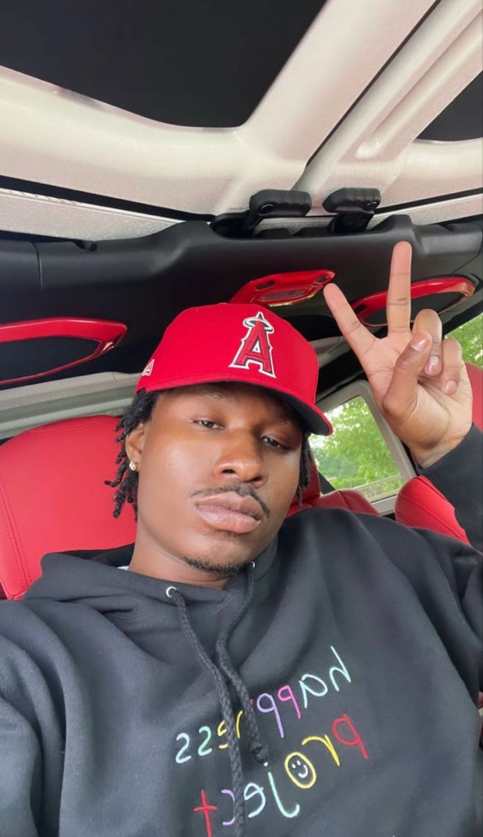 a man sitting in the back seat of a car wearing a red hat and holding up his peace sign