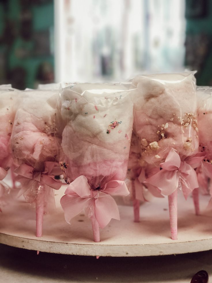 pink marshmallow lollipops are arranged on a white plate with bows and sprinkles