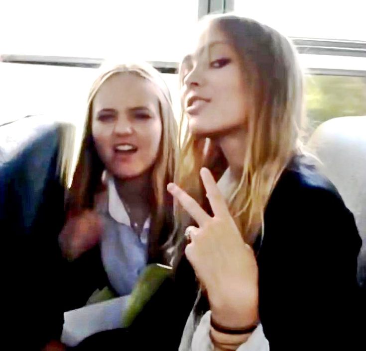 two women sitting on a bus and one pointing at the camera with her finger up