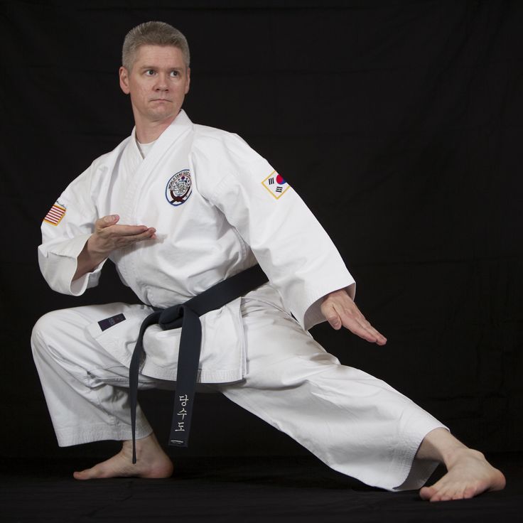 a man sitting on the ground while wearing a white karate suit and black belted pants