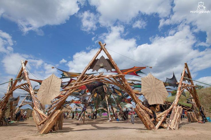 a group of people standing in front of a structure made out of sticks and wood