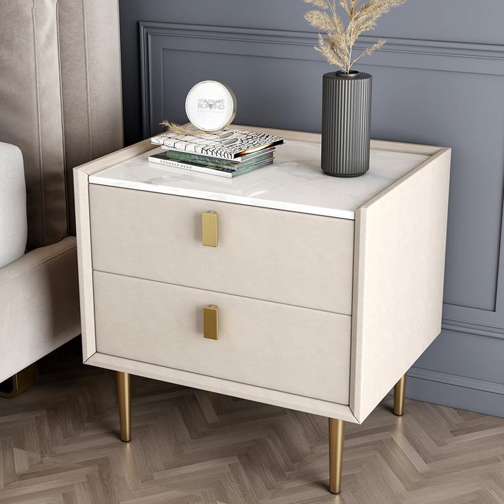 a white nightstand with two drawers and a black vase on the top, next to a couch