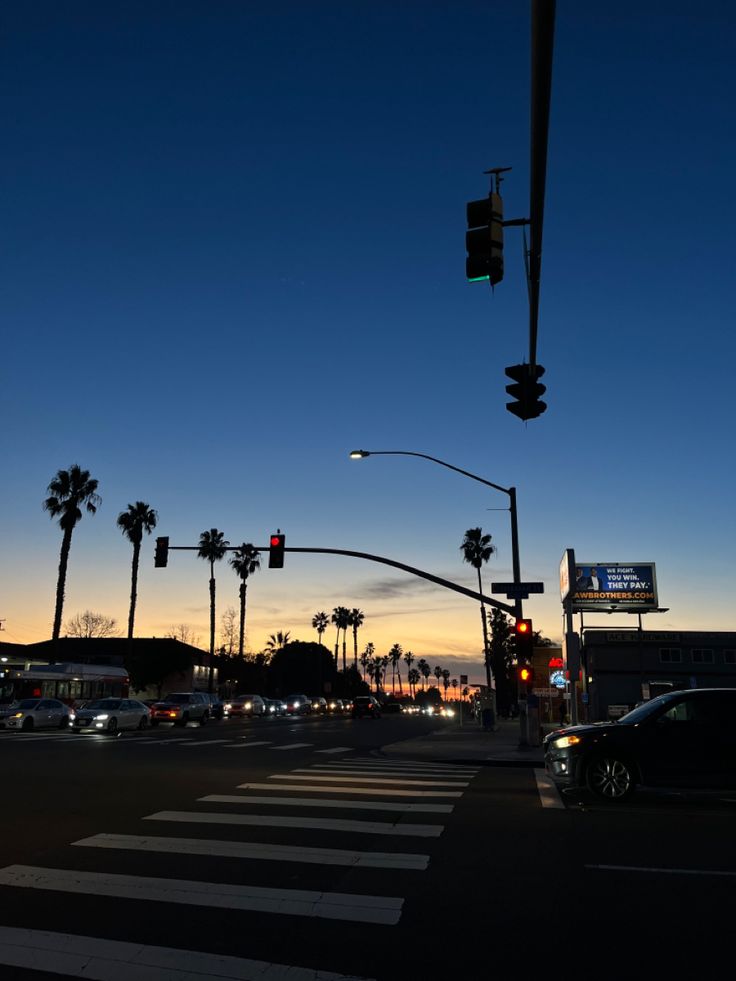 traffic lights and palm trees at dusk on a street in los angeles, california with the sun going down