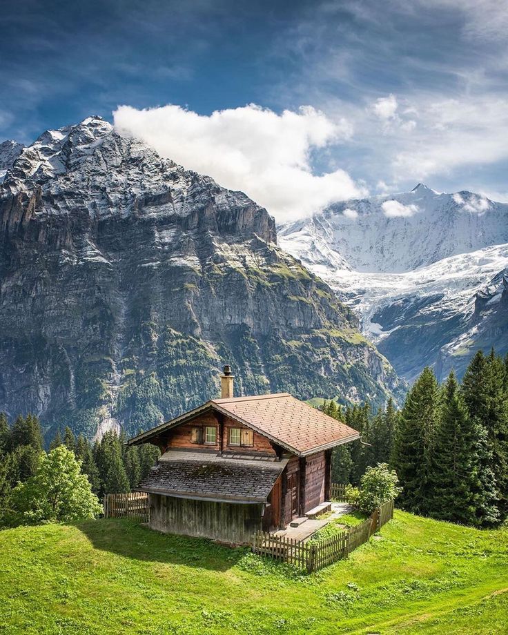 a small cabin in the middle of a green field with mountains in the back ground