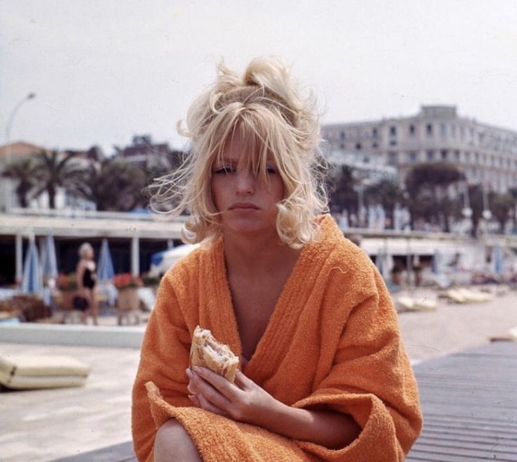 a woman in an orange robe is sitting on a dock and holding a hot dog