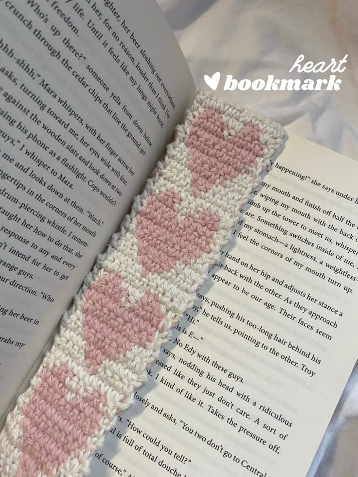 an open book with pink and white crocheted hearts on the cover, next to a knitted ribbon