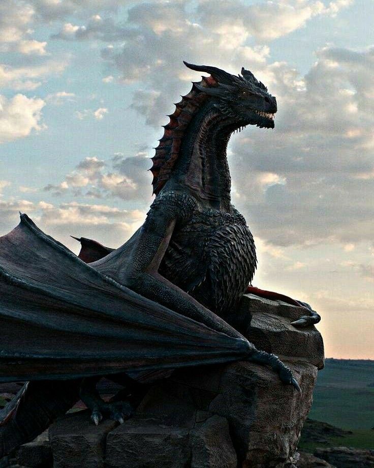 a dragon statue sitting on top of a large rock in front of a cloudy sky