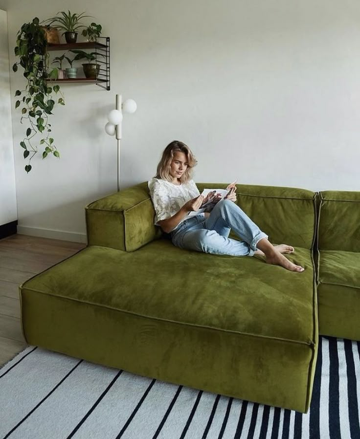 a woman sitting on top of a green couch next to a black and white striped rug