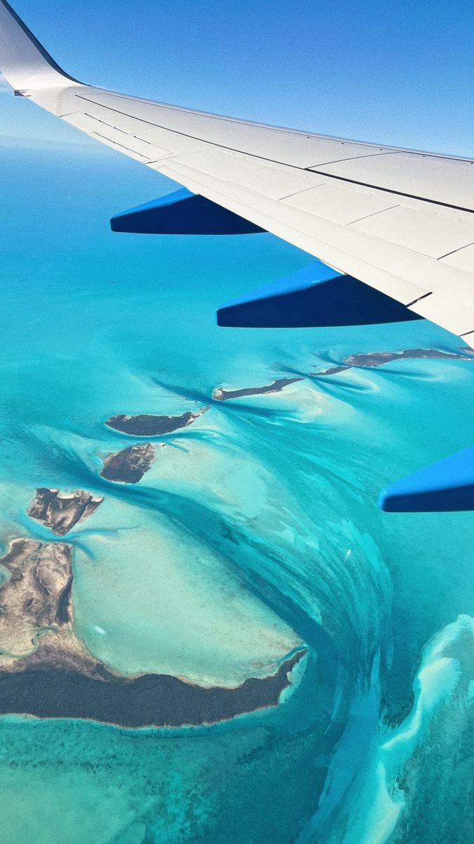 the wing of an airplane flying over some blue water and corals in the ocean