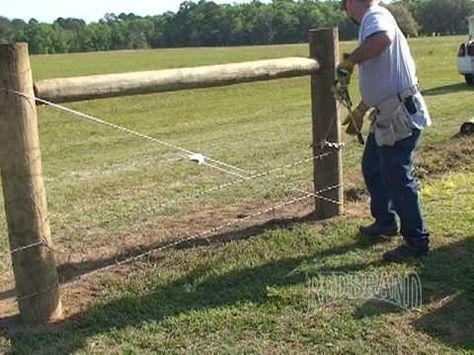 a man standing next to a wooden fence on top of a grass covered field with a truck in the background