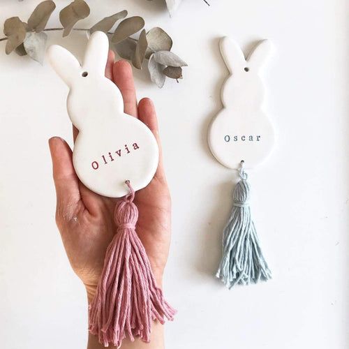 a hand holding two ceramic bunny ornaments with the word avrilo on one and an ostrich on the other